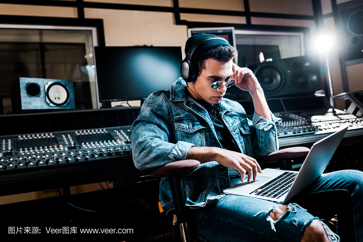 集中混合種族聲音制作人耳機(jī)使用筆記本電腦在錄音室